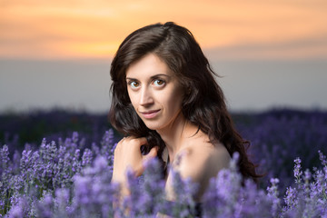 Portrait of a beautiful brunette in a black dress in a lavender field. Sunset in the background.