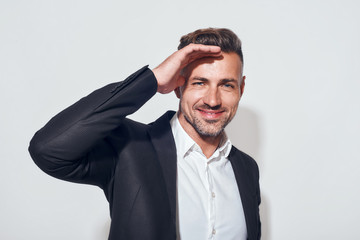 Happy and succesful. Portrait of cheerful bearded businessman in classic suit smiling and looking at camera while standing against grey background