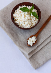 Healthy breakfast, health care. Cottage cheese with fresh green basil in a brown bowl. Wooden spoon with cottage cheese on linen towels. Organic food. Top view at an angle