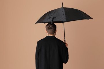 Handsome man with umbrella on color background, back view