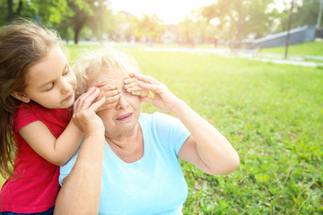 Obraz premium Cute little girl covering eyes of her grandmother in park