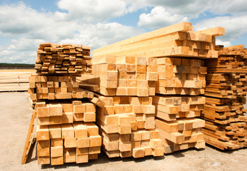 Lumber warehouse in the open air. Wooden beam, planks of wood, stacked in stacks. Sunny day, blue sky with clouds. Horizontal photo
