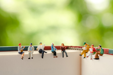 Miniature people, group of business people sitting on a book, doing activity and discussing ideas, society and teamwork concept.