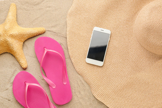 Flip-flops with mobile phone, hat and starfish on sand beach