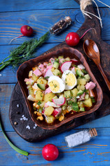Fototapeta na wymiar Russian cold soup Okroshka with vegetables, sausage, eggs and kvass in a bowl on the blue table