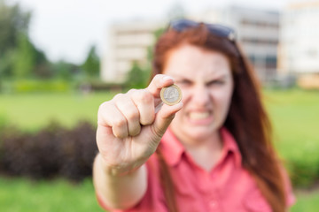 Closeup of woman hand fingers showing one Euro coin, urban green background in summer day. Emotional, young face. Screaming, hate, rage.