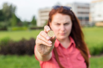 Closeup of woman hand fingers showing fifty euro cents coin, urban green background in summer day. Emotional, young face. Screaming, hate, rage.