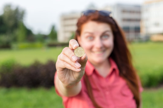 Closeup of beautiful positive friendly-looking young mixed race woman hand fingers showing fifty euro cents coin, urban green background in summer day. Emotional, young face.
