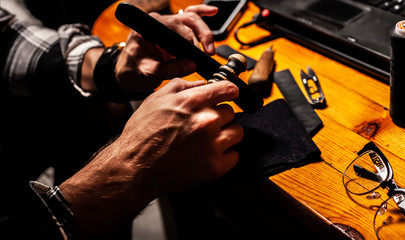 Man makes a leather product, and polishes it in a home workshop. On a wooden table.