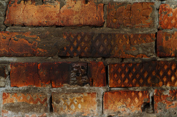 Brickwork, a wall of red-black, uneven bricks. On some bricks, a stencil of curly rhombuses is...