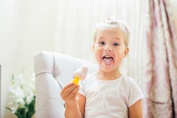 Aborable smiling blonde 3 years baby girl eating homemade ice cream and showing her tongue