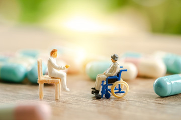 Miniature people: senior patient in wheelchair consulting with doctor, medical healthcare concept.