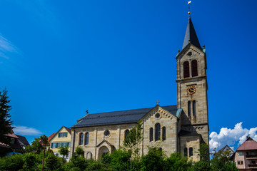 Fototapeta na wymiar Germany, Beautiful ancient church building of kaisersbach near welzheim surrounded by green trees under blue sky