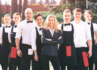 A large group of waiters and waitresses in the open air stand one after another