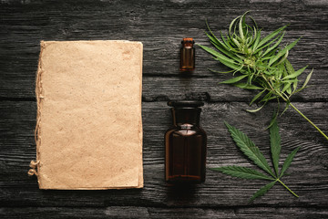 Cannabis cbd oil recipe blank book with a copy space, cbd oil in a bottle and green leaves on a black wooden table background.