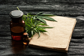 Cannabis cbd oil recipe blank book with a copy space, cbd oil in a bottle and green leaves on a black wooden table background.