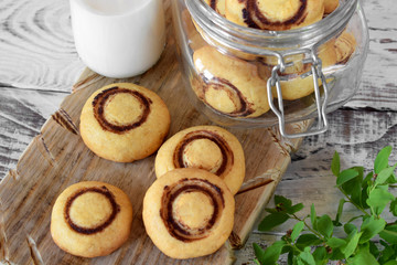 Shortbread champignon-shaped cookies on a wooden board and in a glass jar. A bottle of milk in the background
