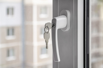 The concept of protecting a child from falling out of windows. Handle with a lock on the window. Apartment house on the background. Closeup, selective focus