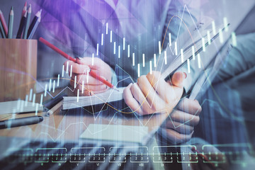A woman hands writing information about stock market in notepad. Forex chart holograms in front....