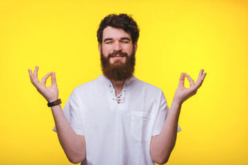 A calm bearded man is  doing zen gesture on yellow background.