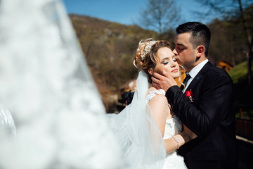 Wind blows veil on bride and groom kising.  Photo of a man and woman in a romantic lovers moment. Fashion photo. Sunny autumn day