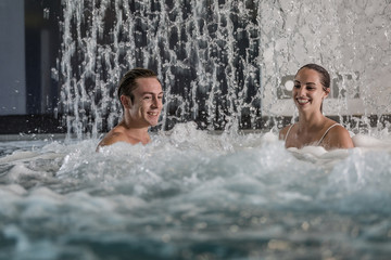 Man and woman under waterfall in foamy pool