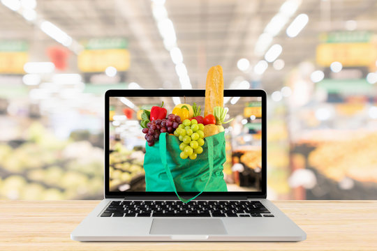 supermarket aisle blurred background with laptop computer and green shopping bag on wood table grocery online concept