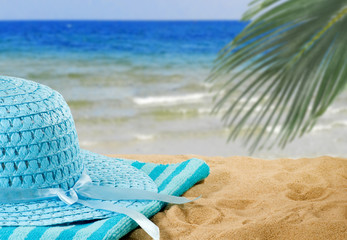 image of a wide-brimmed hat and towel on the sand on the beach against the sea