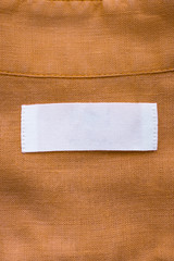 White blank clothing tag label on brown linen shirt fabric texture background