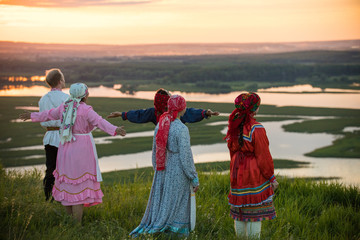 People in traditional russian clothes standing on the field and looking at the sunset