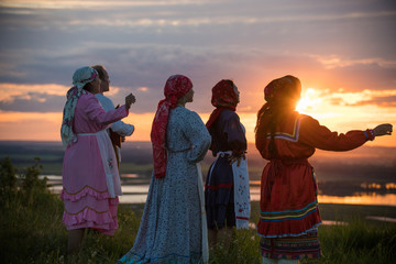 People in traditional russian clothes standing on the field and looking at the bright sunset