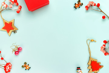 Frame made of red christmas decoration with Christmas tree, star, berries, toy elk and snowman, gift box, earrings on turquoise background. Flat lay, top view