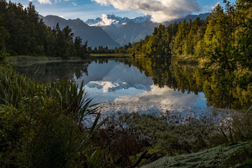 Fototapeta na wymiar A landscape view of the incredibly beautiful Lake Matheson, New Zealand with the reflection of the stunning Southern Alps and the majestic Mt Cook in the still waters, foliage in the foreground