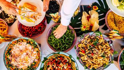 Vertical view of people firends hands taking food from catering table during party celebration - catering and restaurant concept with mixed chef food on a table -coloured background and together