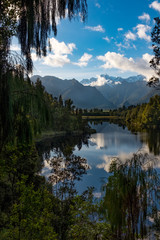 Fototapeta na wymiar A portrait view framed by foliage of the incredibly beautiful Lake Matheson, New Zealand with the reflection of the stunning Southern Alps and the majestic Mt Cook in the still waters.