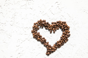 Heart of coffee beans on a white textured background. The concept of good morning.