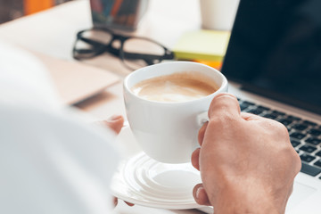 Young businessman working at laptop computer with hot coffee in hand.