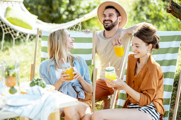 Young friends talking and having fun, while sitting together with summer drinks on the sunbeds at...