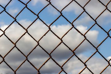 Old rusty mesh netting on a blue sky with clouds, background wallpaper texture.
