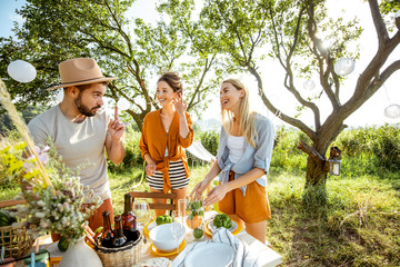 Young and happy friends serving table with food, preparing for the festive lunch in the beautiful...