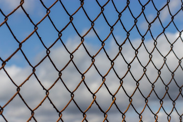 Fototapeta premium Old rusty mesh netting diagonally against a blue sky with clouds, background wallpaper texture