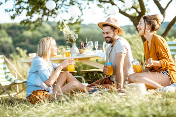 Young friends having fun, sitting together with drinks in the beautifully decorated backyard or...