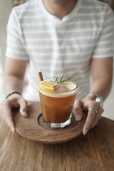 Male hands holding Nitro Orange Cold Brew garnish with rosemary on wooden table