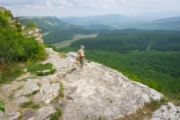 a girl-traveler in a backpack looks into the distance from a cliff on the ruins of a medieval fortified city