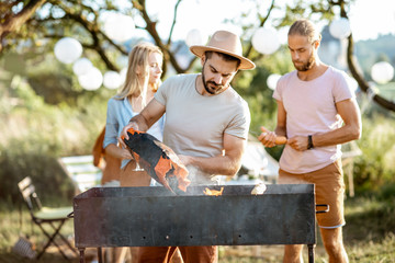 Obraz premium Group of a young friends having barbecue, cooking food in the beautiful garden during a festive lunch on a summer aftenoon