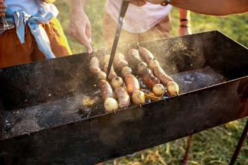 Friends cooking sausages and potatoes on a barbecue outdoors, close-up view