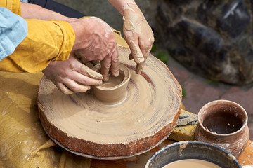 Closeup of the hands of a potter and apprentice.