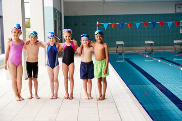 Portrait Of Children Standing On Edge Of Pool Waiting For Swimming Lesson