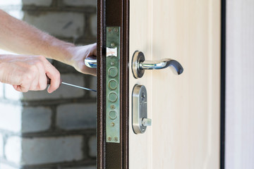 Handyman repair door lock in metal entrance door, Man fixing lock with screwdriver, closeup of repairing door in house.