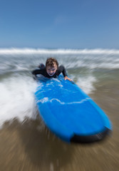 Fototapeta na wymiar Little boy learning to surf at the beach, getting up on surfboard for the first time, motion blur speed effect